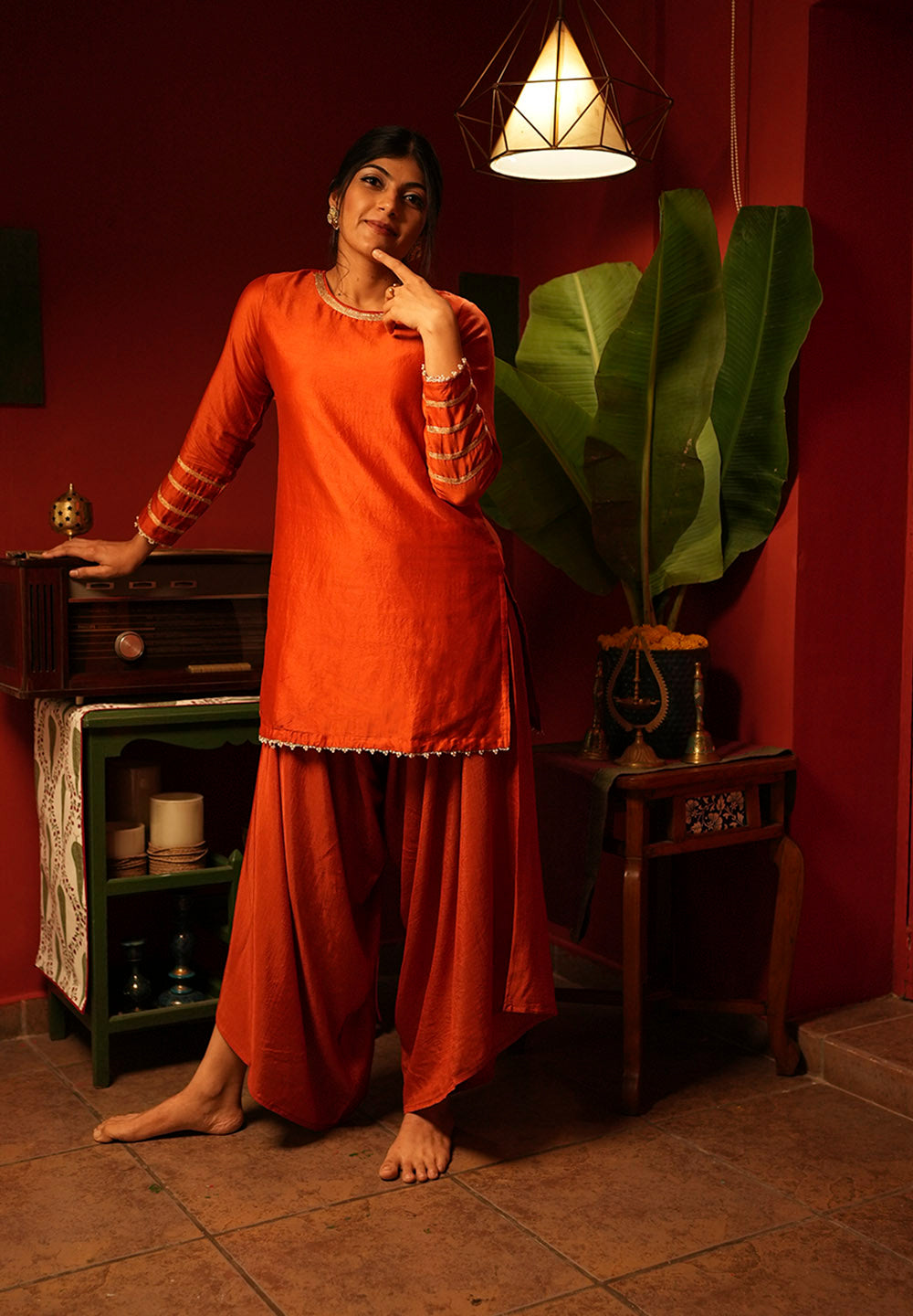 Woman in an orange traditional outfit standing in a room with red walls and decorative elements.