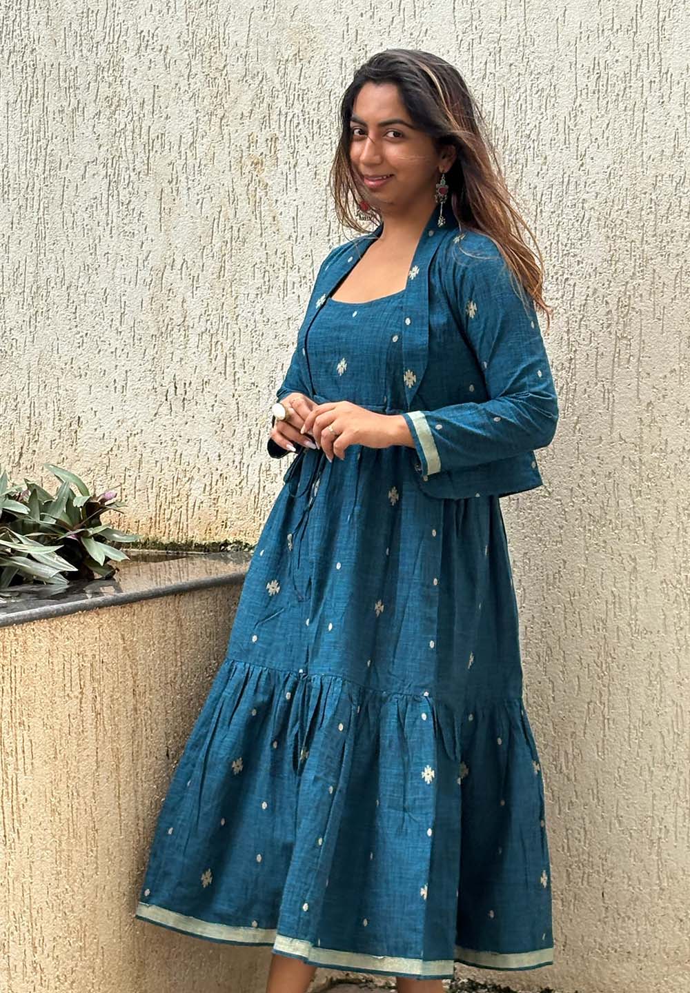 Woman wearing a blue dress with white patterns against a textured wall.
