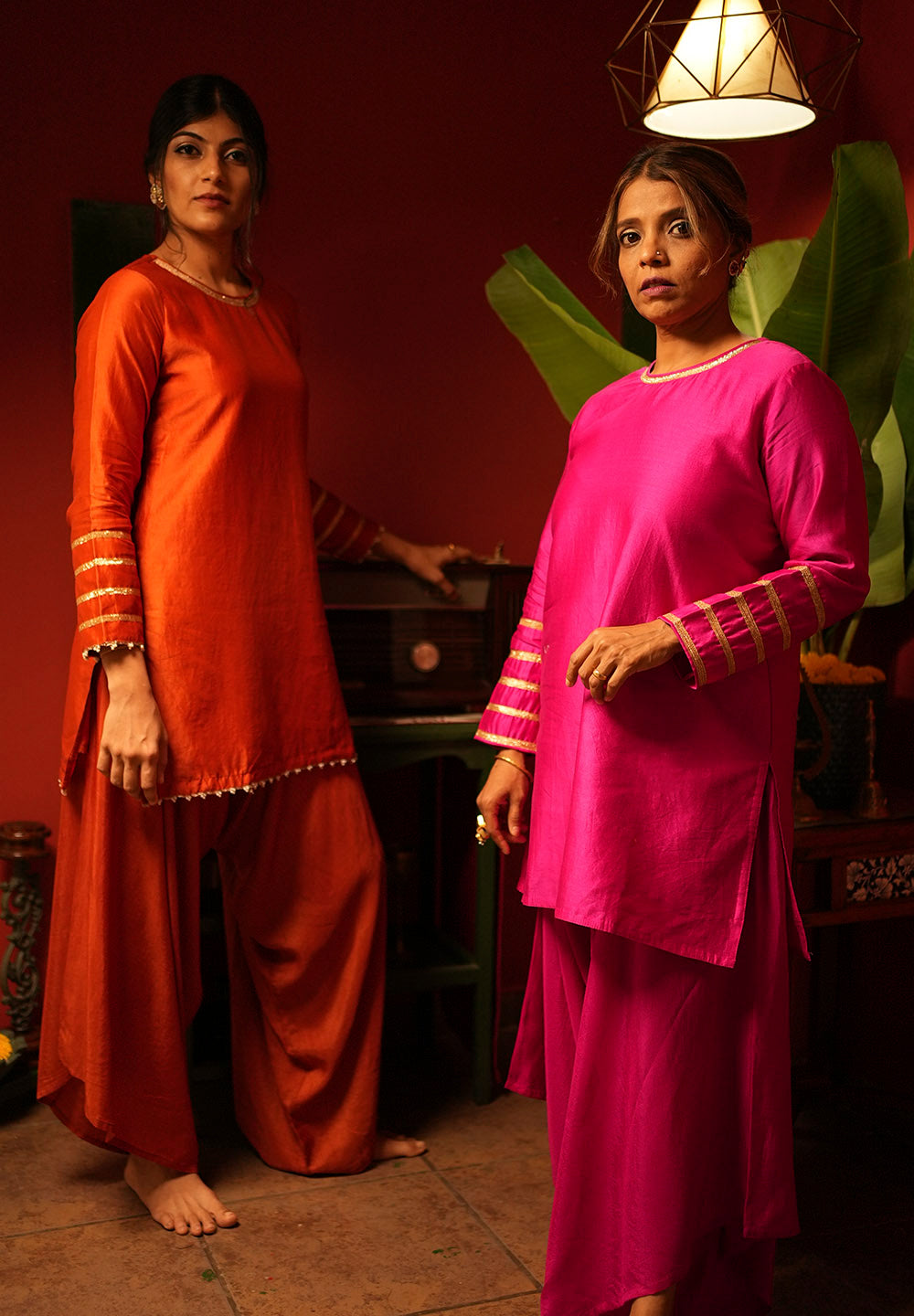 Two women in traditional outfits standing indoors with a warm ambiance.