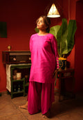 Woman in a bright pink outfit standing in a room with a red wall, green plant, and vintage radio.