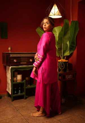 Woman in a bright pink traditional outfit standing in a room with a vintage radio and plants.